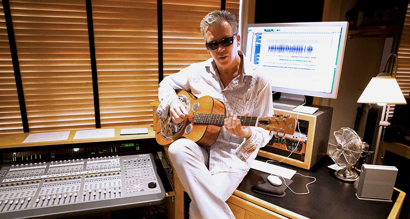 Simon Climie playing an acoustic guitar in a mixing studio in front of a computer screen with Pro Tools displayed Simon Climie playing an acoustic guitar in a mixing studio in front of a computer screen with Pro Tools displayed